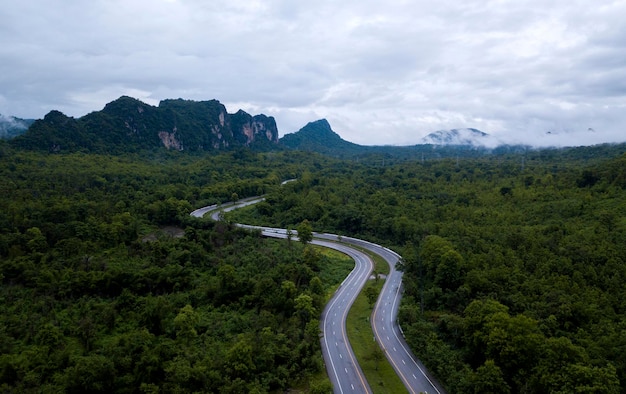 Top view of countryside road passing through the green forrest and mountain