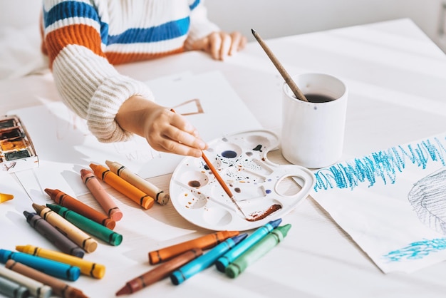 Top view cropped image of cute little girl painting and drawing with brush and watercolor on white desk at home Pretty preschool kid draws in the kindergarten People childhood and education concept