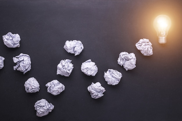 Top view crumpled white paper and light bulbs on black stone board