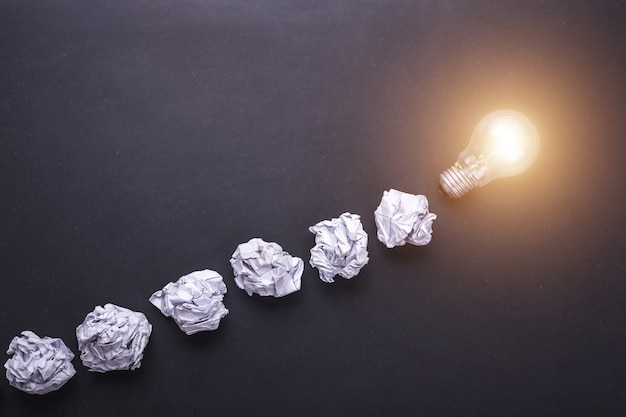 Top view crumpled white paper and light bulbs on black stone board