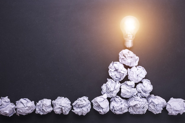 Top view crumpled white paper and light bulbs on black stone board