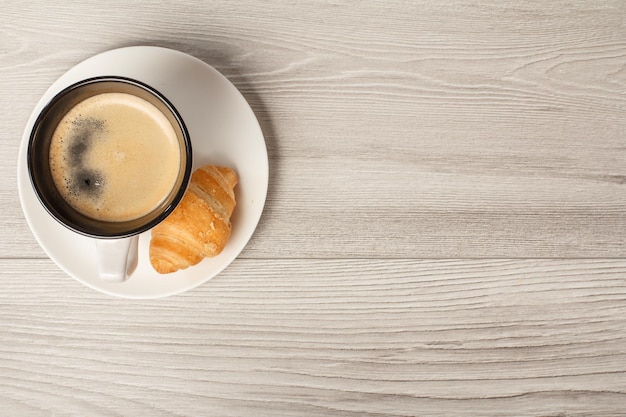 Top view of cup of black coffee with fresh croissant on saucer