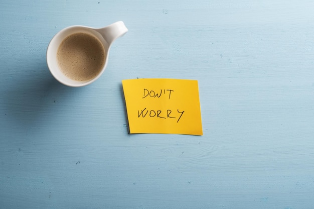 Top view of a cup of caffe latte placed next to a yellow paper with Dont worry sign