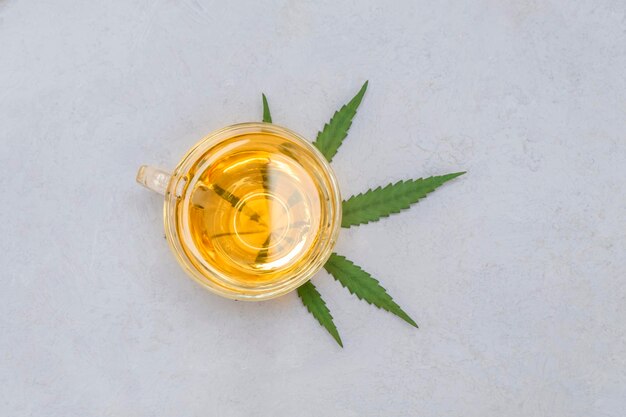 Top view of cup of cannabis tea with green marijuana leaf on neutral grey background copy space