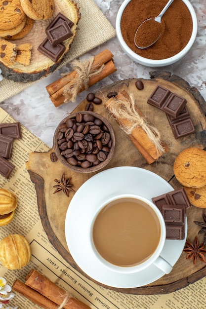 top view cup of coffee biscuits bowl with roasted coffee beans chocolate cinnamon sticks anise stars on wood board cocoa bowl on table