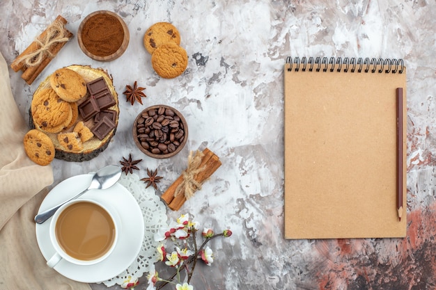 top view cup of coffee bowl with roasted coffee beans and cocoa chocolate cinnamon sticks biscuits notebook and pencil on table