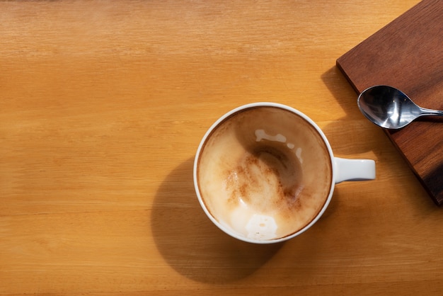 Top view cup of coffee has been drunk with spoon on brown wooden table with copy space for text