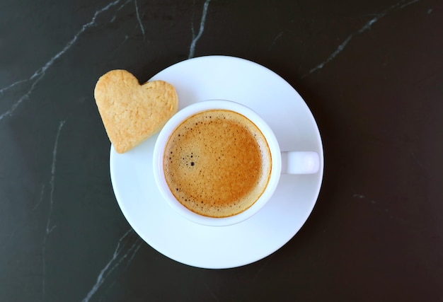 Top View of a Cup of Coffee with Heart Shaped Cookie on Black Backdrop