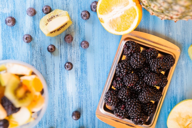 Top view of a cup full of delicious fruits over a wooden desk. Berry, banana, kiwi and grapes over blue table