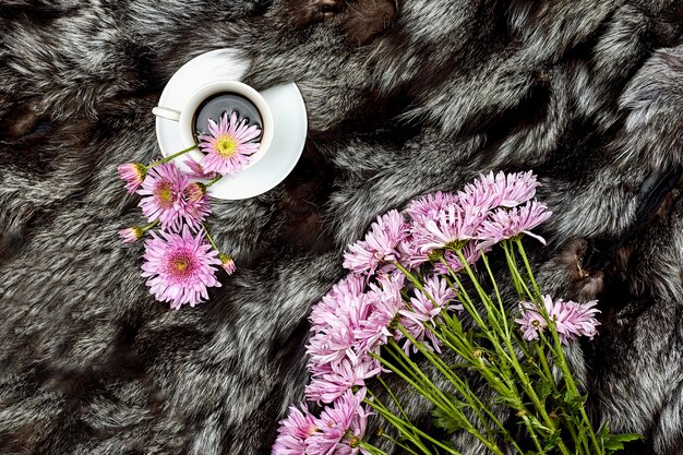 Top view of a cup of hot black coffee on fur rug with fresh spring flowers