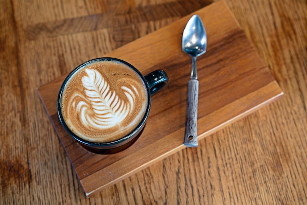 Top view a cup of hot coffee cappuccino latte art with Teaspoon on wooden plate.