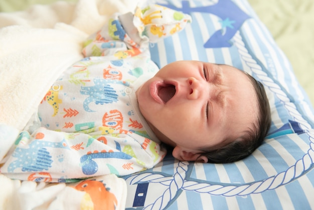 Top view of cute little Asian baby yawning before sleep on the bed