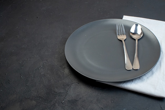 Top view of cutlery set on black plate on white towel on dark color background with free space