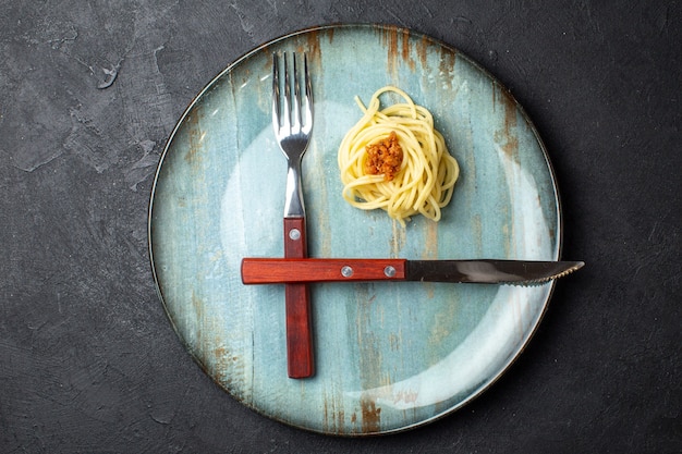 Top view of cutlery set and pasta meal with meat on blue plate on black background with free space