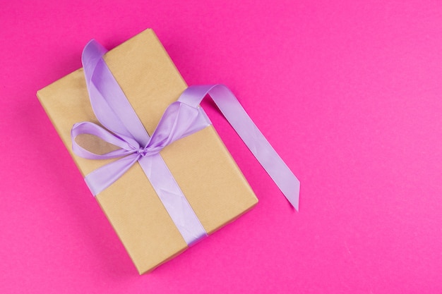 Top view of a decorated present with a bow on pink background