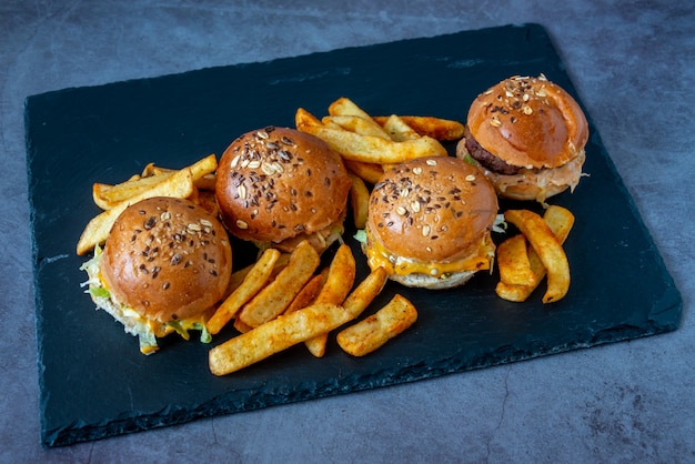 Top view of delicious cheeseburgers and fries on a black serving board