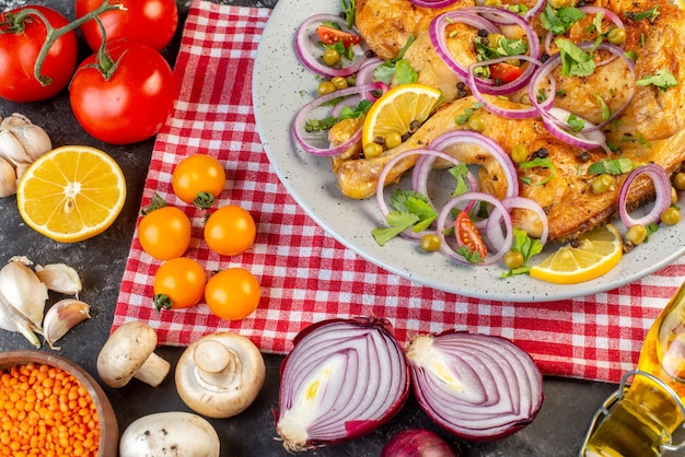 Top view of delicious dinner fried chicken dish with various spices and foods tomatoes with stems red lentil garlics fallen oil bottle lemon mushrooms on dark color background