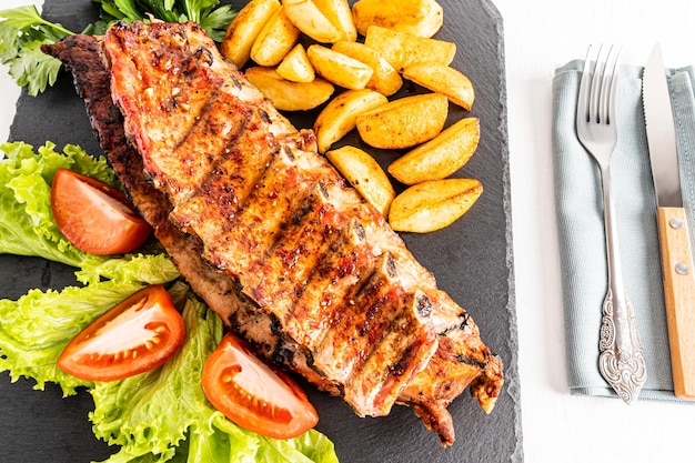 Top view of the delicious juicy grilled pork ribs with potato slices and salad on a slate board Cutlery delicious food