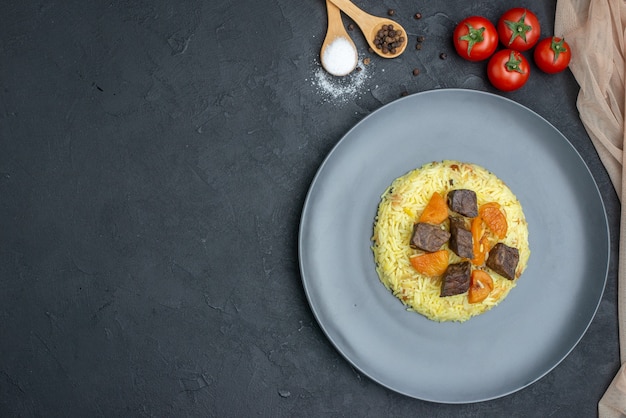 Top view delicious pilaf cooked rice with meat slices and tomatoes on dark surface