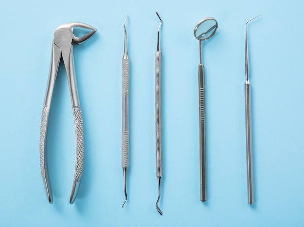 Top view of dental tools set on blue table in dentists clinic: dental mirror, explorers, forceps.