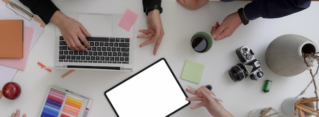 Top view of designer team working together in minimal meeting room with mock-up tablet, laptop, camera and designer supplies