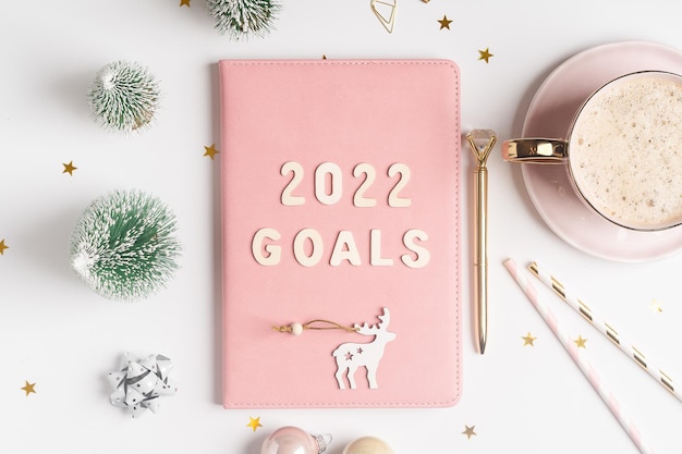 Top view desktop christmas pink notepad with goals letters text flat lay of white table background