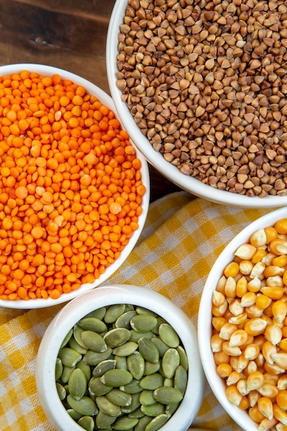 top view different raw ingredients rice corns lentils and buckwheat in plates on brown surface