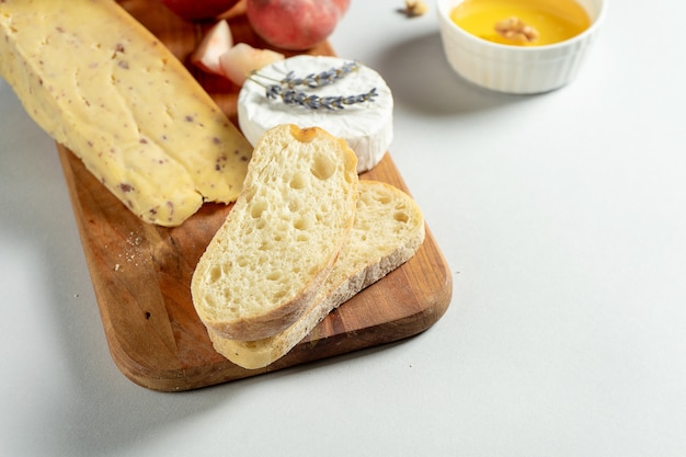 Top view different types of cheeses on wooden cutting board. Cheese with fig peach, honey, ciabatta and nuts, glass of red wine. Stylish food flat lay on grey background. Copy space. Soft focus