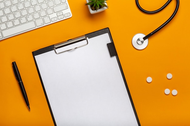 Top view of doctor's desk with stethoscope keyboard notepad and pen, prescription and pills