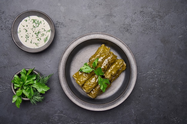 Top view dolma parsley saucepan with sour cream on ceramic color graphite plate on dark table close