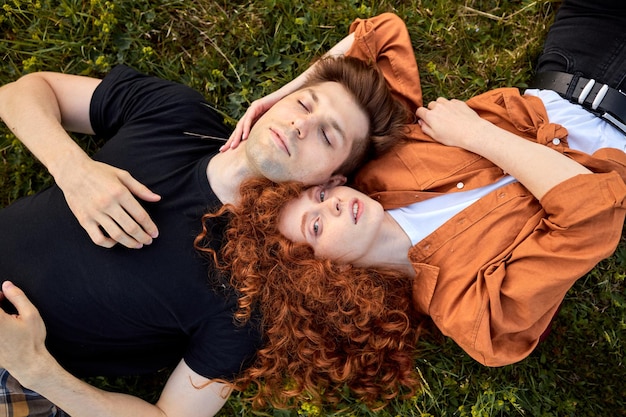 Top view on dreamy couple lying on grass in field at summer day, enjoying nature