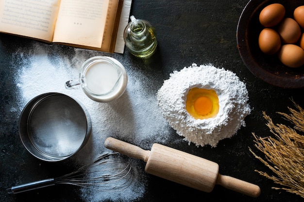 Top view eggs, dough, flour and rolling-pin on the stone table background. Free space for text .