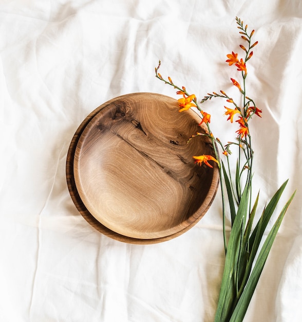 Top view of empty brown round handmade wooden bowls and orange flowers on white cotton tablecloth. Flat lay. copy sapce