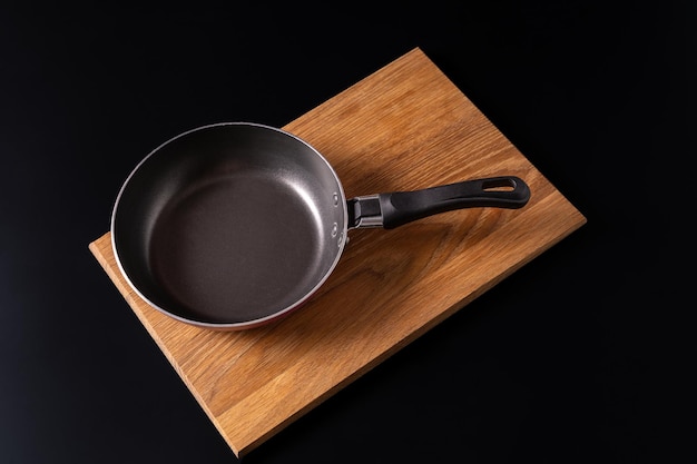 Top view of an empty frying pan on a wooden chopping board isolated on a black background