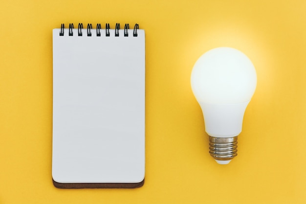 Top view of empty open lined notebook and LED light bulb on yellow background ideas concept