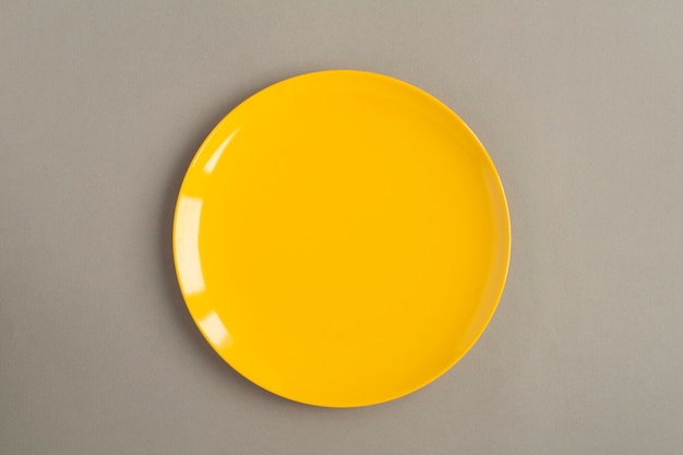 Top view of empty yellow plate on the gray background