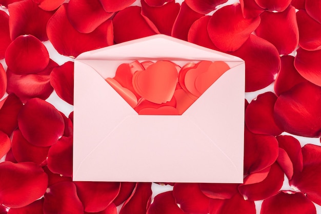 Top view of envelope with heart shaped confetti and red rose petals on background st valentines day