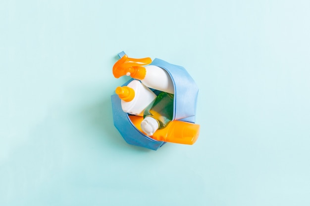 Top view of female cosmetics bag full of suncream spray, sunsreen, sunblock and body lotion and spf cream on blue background with copy space. Directly above. Bright summer concept.