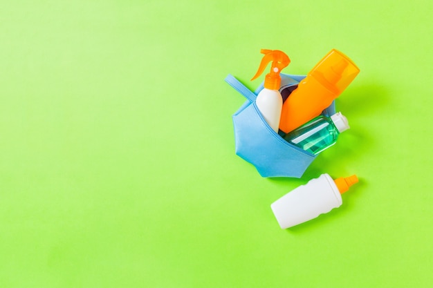 Top view of female cosmetics bag full of suncream spray, sunsreen, sunblock and body lotion and spf cream on green background with copy space. Directly above. Bright summer concept.