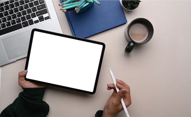 Top view of female designer hand holding digital tablet with blank screen and stylus pen at her workspace.