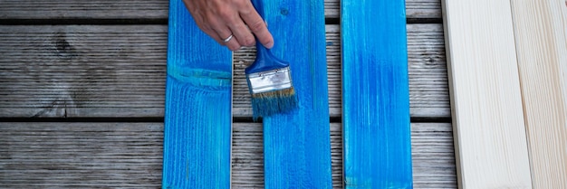 Top view of female hand painting wooden planks with blue paint using a brush Wide view image