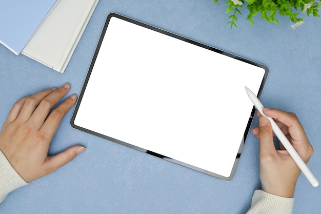 Top view of a female hand using stylus pen drawing on digital tablet in minimal blue workspace