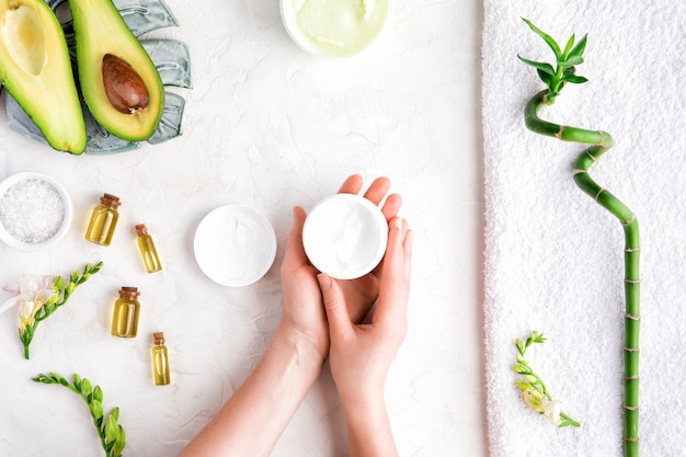 Top view of female hands applying hand cream. Flat lay of bamboo, avocado oil, cream - skincare concept