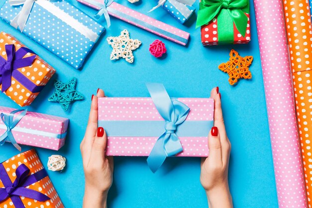 Top view of female hands holding a Christmas present on festive blue background Holiday decorations and wrapping paper New Year holiday concept