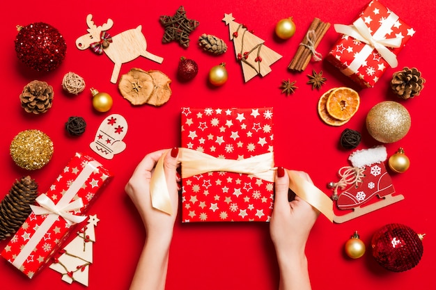 Top view female hands holding a Christmas present on festive red . Holiday decorations.   holiday 