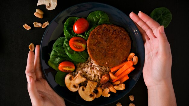 Photo top view of female hands holding a plate of vegan plant based food vegan meatless cutlet and ric