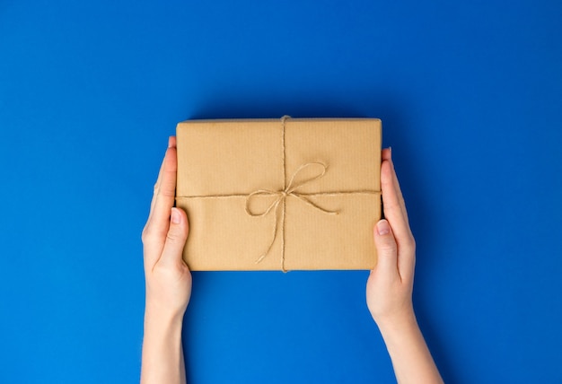 Top view of female hands holding present box package on Blue background. Zero waste shopping concept. Flat lay banner, top view, Sustainable lifestyle. 