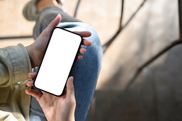 Top view A female holding a smartphone white screen mockup over blurred background