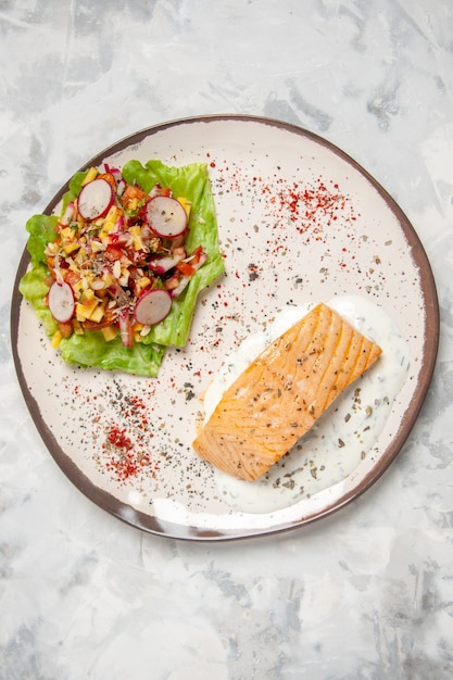 Top view of fish meal and delicious salad on a plate on stained white surface