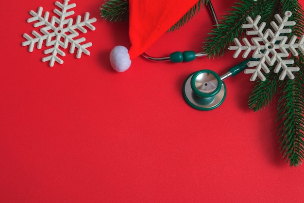 Top view of flat Christmas decorations and stethoscope on red background. Concept for medical announcement, banner. With copy space